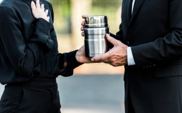cropped view of man and woman holding mortuary urn in graveyard